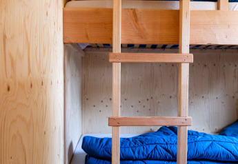 Ein Etagenbett aus Holz mit blauer Bettwäsche in einer kleinen Kabine in Jachthut, Camping Vinkenhof, Niederlande.
