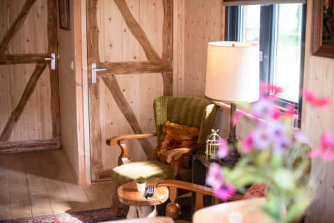 Rincón acogedor en la tiny house Jachthut de Camping Vinkenhof, con sillón, lámpara y paredes de madera.