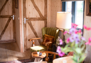 Coin salon chaleureux de la tiny house Jachthut à Camping Vinkenhof, avec fauteuil, lampe et murs en bois.