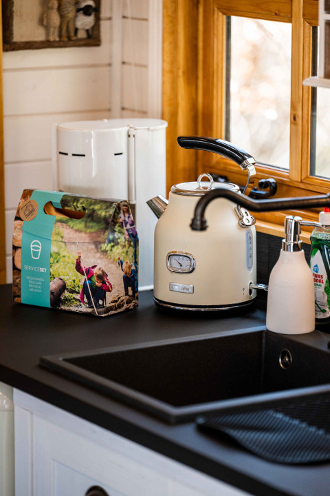 Kitchen countertop at Shepperd Lodge with kettle, soap dispenser, dish set and window, in glamping style.