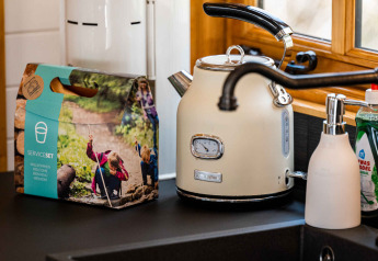 Kitchen countertop at Shepperd Lodge with kettle, soap dispenser, dish set and window, in glamping style.