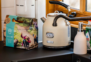 Kitchen countertop at Shepperd Lodge with kettle, soap dispenser, dish set and window, in glamping style.