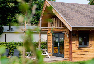 Petite cabane en bois Jachthut au Camping Vinkenhof, Pays-Bas, entourée d’arbres verts et pelouse d’été.