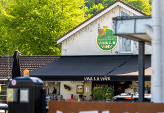 Uitzicht op Café Restaurant Viva La Vink bij Camping Vinkenhof, omgeven door bomen in Limburg, Nederland.