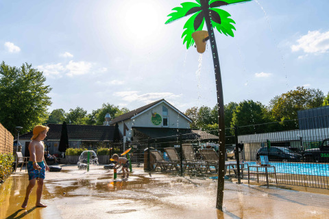 Des enfants jouent sous un palmier arroseur près de la piscine au Camping Vinkenhof, Limbourg, Pays-Bas.