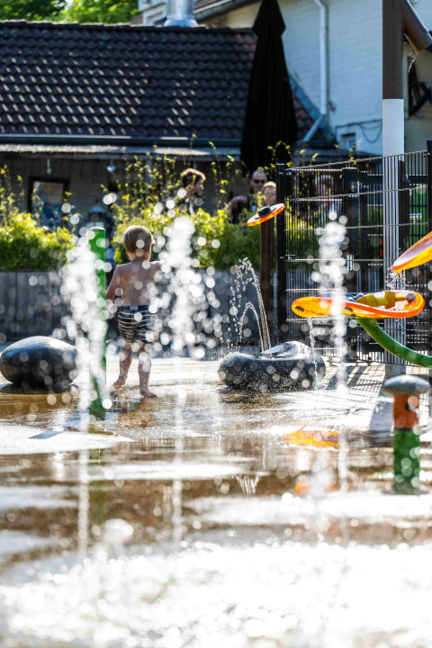 Child playing among water fountains at the splash playground of Camping Vinkenhof in Limburg, Netherlands.