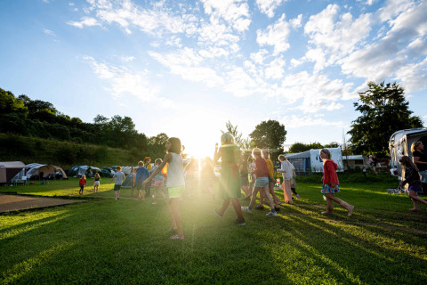 Bambini giocano sull’erba soleggiata al Camping Vinkenhof, parco vacanze in Limburgo, Paesi Bassi, tra tende.