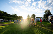Bambini giocano sull’erba soleggiata al Camping Vinkenhof, parco vacanze in Limburgo, Paesi Bassi, tra tende.
