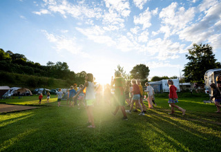 Bambini giocano sull’erba soleggiata al Camping Vinkenhof, parco vacanze in Limburgo, Paesi Bassi, tra tende.