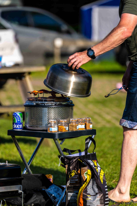 Outdoor cooking at Camping Vinkenhof with a grill, spice jars and a beer can on a folding table.