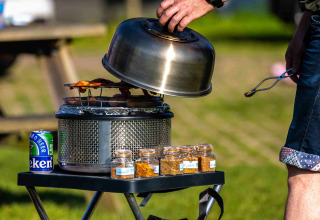Cucina all'aperto al Camping Vinkenhof con griglia, barattoli di spezie e lattina di birra.