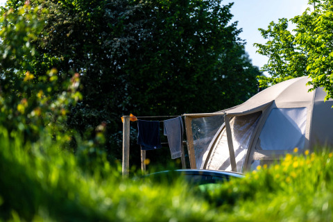 Tienda con tendedero y ropa rodeada de verde en Camping Vinkenhof, Limburgo, Países Bajos, día soleado.