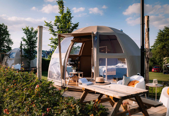 Panorama Dome luxury glamping tent with outdoor wooden patio, picnic table, seating, and scenic garden view.