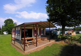 Safari tent Tentlodge at Camping Vinkenhof in the Netherlands, with wooden deck, picnic table and green field.