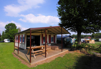 Safari tent Tentlodge at Camping Vinkenhof in the Netherlands, with wooden deck, picnic table and green field.