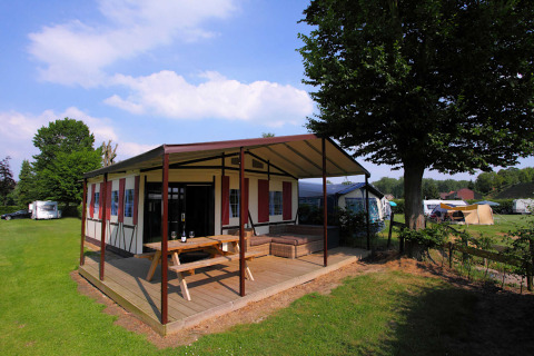 Safari tent Tentlodge at Camping Vinkenhof in the Netherlands, with wooden deck, picnic table and green field.