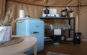 Pequeña cocina en el Panorama Dome en Camping Vinkenhof, Países Bajos, con nevera azul y estantería.
