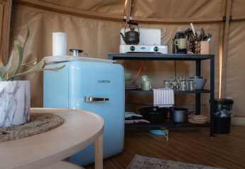 Pequeña cocina en el Panorama Dome en Camping Vinkenhof, Países Bajos, con nevera azul y estantería.