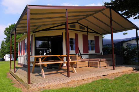 Safari tent lodge with covered wooden terrace, picnic table, and outdoor seating at Camping Vinkenhof, Netherlands.