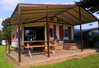Tenda lodge safari con terrazza in legno coperta, tavolo da picnic e divani al Camping Vinkenhof nei Paesi Bassi.