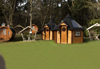 Tiny log cabins and a wine barrel house on green grass at Costa Kabrita, Netherlands, surrounded by forest.
