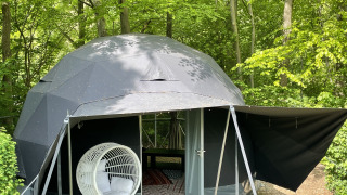 Geodætisk Dome Tent i en skov, med en hvid hængestol udenfor og grønne træer omkring teltet.