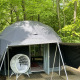 Geodætisk Dome Tent i en skov, med en hvid hængestol udenfor og grønne træer omkring teltet.