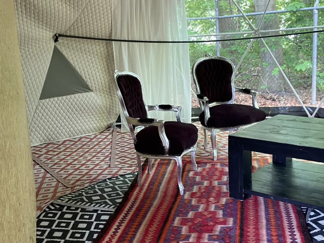 Interieur van de Dome Tent bij Buytenplaets Abelen in Nederland, met luxe stoelen en kleurrijke tapijten.