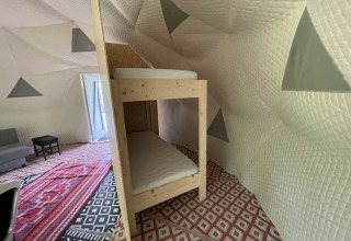 Binnenkant van Dome Tent bij Buytenplaets Abelen, Nederland, met stapelbed, tapijten en gewatteerde muren.