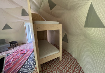 Inde i Dome Tent ved Buytenplaets Abelen, Holland, ses køjeseng, farverige tæpper og quiltede vægge.
