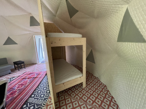 Interno della Dome Tent presso Buytenplaets Abelen, Paesi Bassi, con letti a castello e tappeti a motivi.