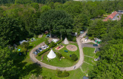 Luftfoto af glampingplads omgivet af skov, med telte, biler, stier og rekreative områder i naturen.