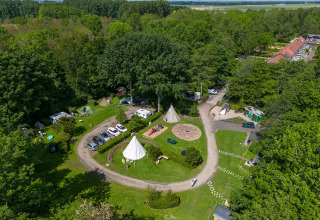 Vista aérea de un alojamiento glamping rodeado de bosque, con tiendas, coches, caminos y áreas recreativas.