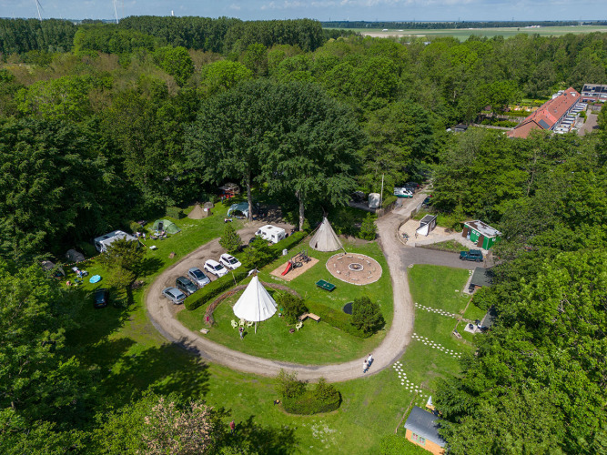 Luchtfoto van een glamping-accommodatie in het bos met tenten, auto’s, paden en recreatiegebieden.