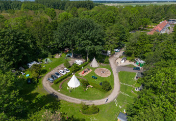 Luftfoto af glampingplads omgivet af skov, med telte, biler, stier og rekreative områder i naturen.