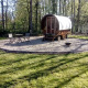 Et billede af en Gipsy Wagon tiny house i skoven, med et lille bord og to stole på en grusplads.
