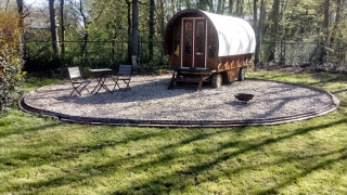 Een Gipsy Wagon tiny house in het bos, met een tafeltje en twee stoelen op een cirkel van grind.