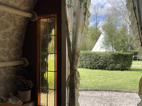 Udsigt fra Gipsy Wagon ved Buytenplaets Abelen i Holland med tipi, grøn hæk og blomstrede gardiner.