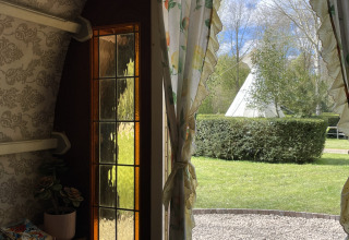 Vista desde el Gipsy Wagon en Buytenplaets Abelen, Países Bajos, con tipi y cuidados setos al aire libre.