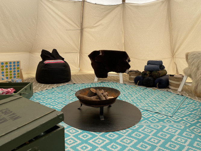 Intérieur d’un tipi à Buytenplaets Abelen, Pays-Bas, avec feu, tapis et sièges confortables.