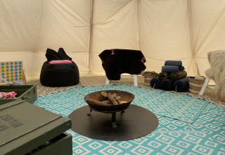 Interior de una tienda tipi en Buytenplaets Abelen, Países Bajos, con fogón, alfombras y asientos.
