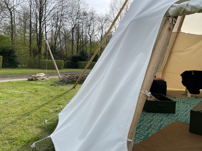Vue depuis l'entrée d'un tipi à Buytenplaets Abelen, Pays-Bas, montrant pelouse et arbres à l'extérieur.
