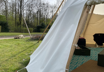 Vista desde la entrada de una tienda tipi en Buytenplaets Abelen, Países Bajos, con césped y árboles afuera.