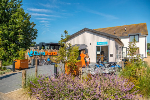 Immagine esterna della reception del villaggio vacanze EuroParcs con biciclette, ospiti e fiori.