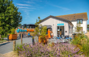 Udendørsbillede af EuroParcs ferieparkens reception med cykler, planter og gæster i sommervejr.