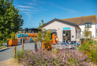 Vue extérieure de la réception du parc de vacances EuroParcs avec vélos, fleurs et visiteurs en été.