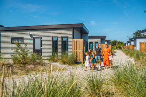 Una familia pasea junto a modernas cabañas glamping en un parque de vacaciones rodeado de naturaleza.