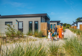 Een gezin wandelt langs moderne glampingaccommodaties in een vakantiepark vol groen en natuur.