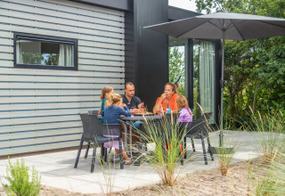 Een familie geniet van een maaltijd onder een grote parasol op het terras van een glamping vakantiepark.