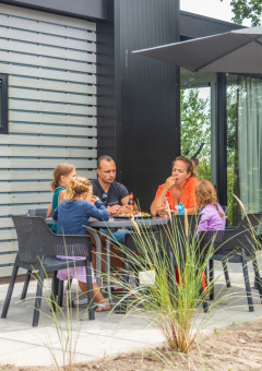 Una familia disfruta de una comida al aire libre en un parque de vacaciones con glamping, bajo una sombrilla grande.